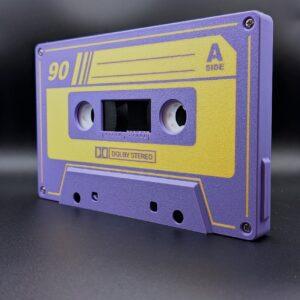 Iconic Audio Cassette: An LED Nightlight features a retro design with purple and yellow hues, labeled 90 and A Side, complete with authentic Dolby Stereo text against a sleek black background. This captivating piece pays homage to the golden era of analog audio, enhanced with intricate reel-to-reel details and brushed aluminum-like accents reminiscent of vintage tape decks. The cassette-inspired nightlight offers an immersive glow that emulates the soft ambiance of VU meters dancing to your favorite tunes.