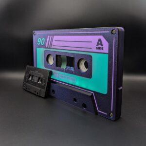 Two audio cassettes rest on a dark backdrop: the larger one showcases the Iconic Audio Cassettes vibrant purple, green tricolor LED nightlight design, emphasizing its retro aesthetic with advanced illumination technology. Meanwhile, the smaller cassette sports a sleek black exterior with crisp white lettering, reminiscent of classic analog style. Both tapes evoke a sense of nostalgia while highlighting high-fidelity sound technologies and magnetic tape innovation.