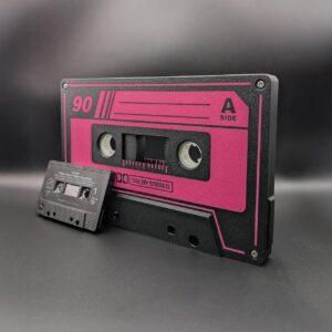 Oversized black retro cassette tape with vibrant pink design and optional LED lightbox, shown next to a standard cassette for scale