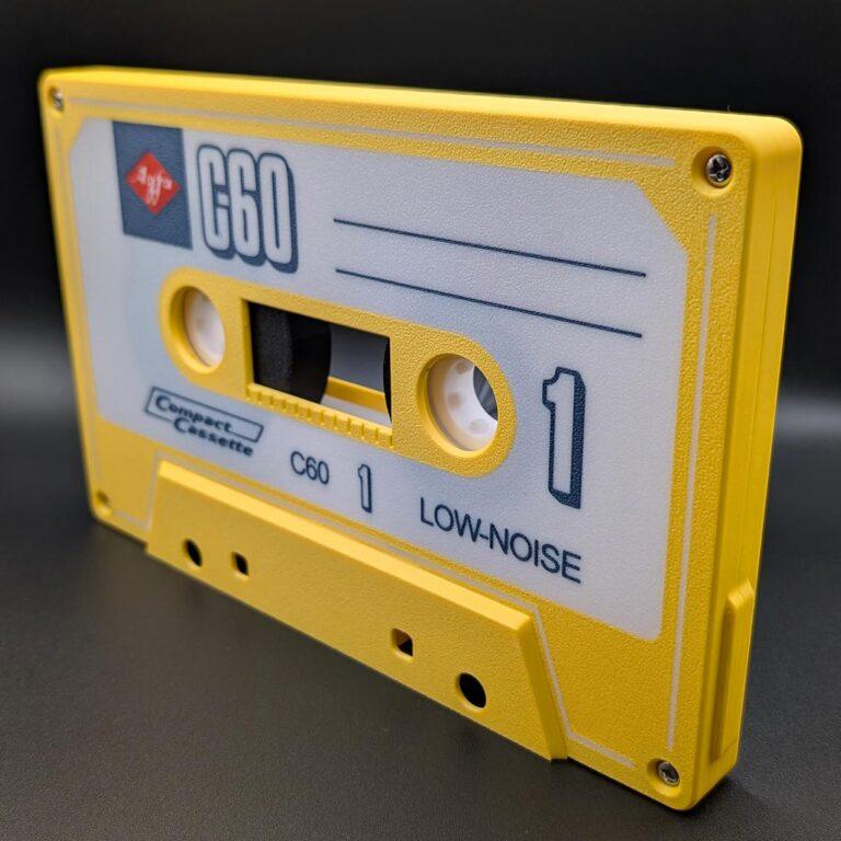 The iconic AGFA audio cassette, featuring a yellow and white design with LOW-NOISE labeling lines, is set against a black background. This classic tape reel encapsulates vintage analog charm with its precision-wound magnetic tape and robust shell construction. The front showcases a sleek case window, offering a glimpse of the intricately engineered spools inside. Each cassette promises superior wow and flutter performance, ideal for audiophiles who appreciate dynamic range and rich tonal fidelity in their playback experience.