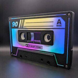 A vintage cassette tape labeled 90 on the A side, featuring a vibrant gradient design with text indicating Dolby Stereo encoding and chromium dioxide (CrO2) formulation for enhanced sound quality. The tape includes high-fidelity ferrite particles for superior audio clarity. Its set against a dark background that highlights the gleaming metallic reels and precision-engineered head gaps.