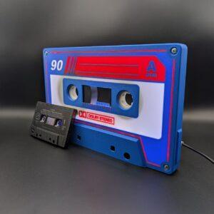 The Iconic Audio Cassette | Blue White Red | LED Nightlight, looks like a jumbo tape deck cassette with an A SIDE label and sits next to a standard black audio cassette on a matte black soundstage backdrop.