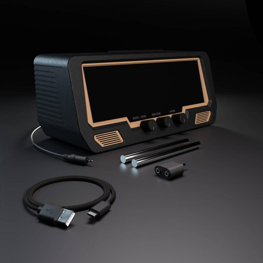 The Audio Visualizer Pro, a sleek black audio unit with a blank display, is shown with three pen-style touch styluses, an audio interface charging cable, and two mini jack adapters on a dark soundstage surface.