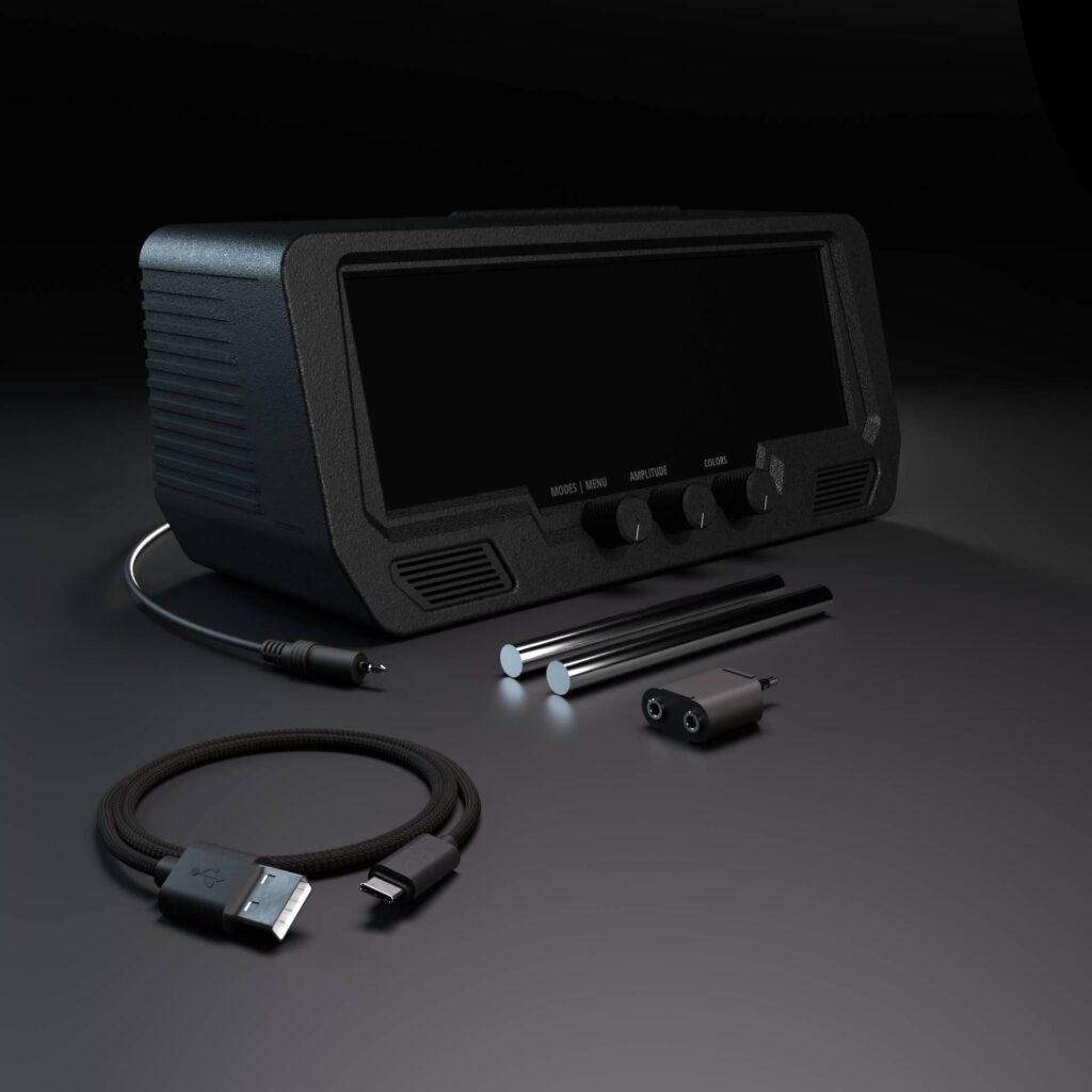 The Audio Visualizer Pro, a black electronic tablet with a blank screen, is shown with a power cord, USB cable, audio jack, two styluses, adapter, and mixer cable on a dark surface.
