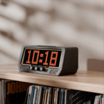 A digital alarm clock displaying 10:18 sits on a wooden shelf above vinyl records, a retro cassette, and vintage speakers.