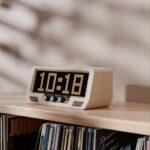 A digital clock displaying 10:18 sits on a wooden shelf above vinyl records, flanked by speakers and headphones in the retro audio setup.