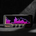 The Audio Visualizer Pro, with a black chassis, displays purple LED sound wave bars on its LCD panel atop a gray studio rack.