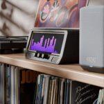 An Audio Visualizer Pro with a colorful equalizer display sits on a shelf near a Denon speaker, vinyl records, and hi-fi amp.