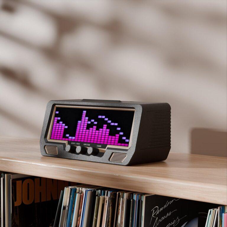 A digital audio player with a vibrant LED equalizer display rests on a wooden shelf above vinyl records, speakers, and a signed album cover.