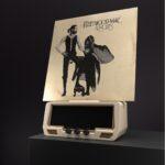 A Fleetwood Mac Rumours vinyl record is propped upright on a retro hi-fi radio receiver resting on a dark tabletop.