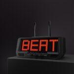 A digital clock radio on a dark surface displays BEAT in bold red LED letters, flanked by two metallic antenna rods on top.