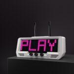 A retro-style digital radio with vinyl sleeve support, built-in microphone, knobs, and an LED sound visualizer displays PLAY in bright pink on its screen.
