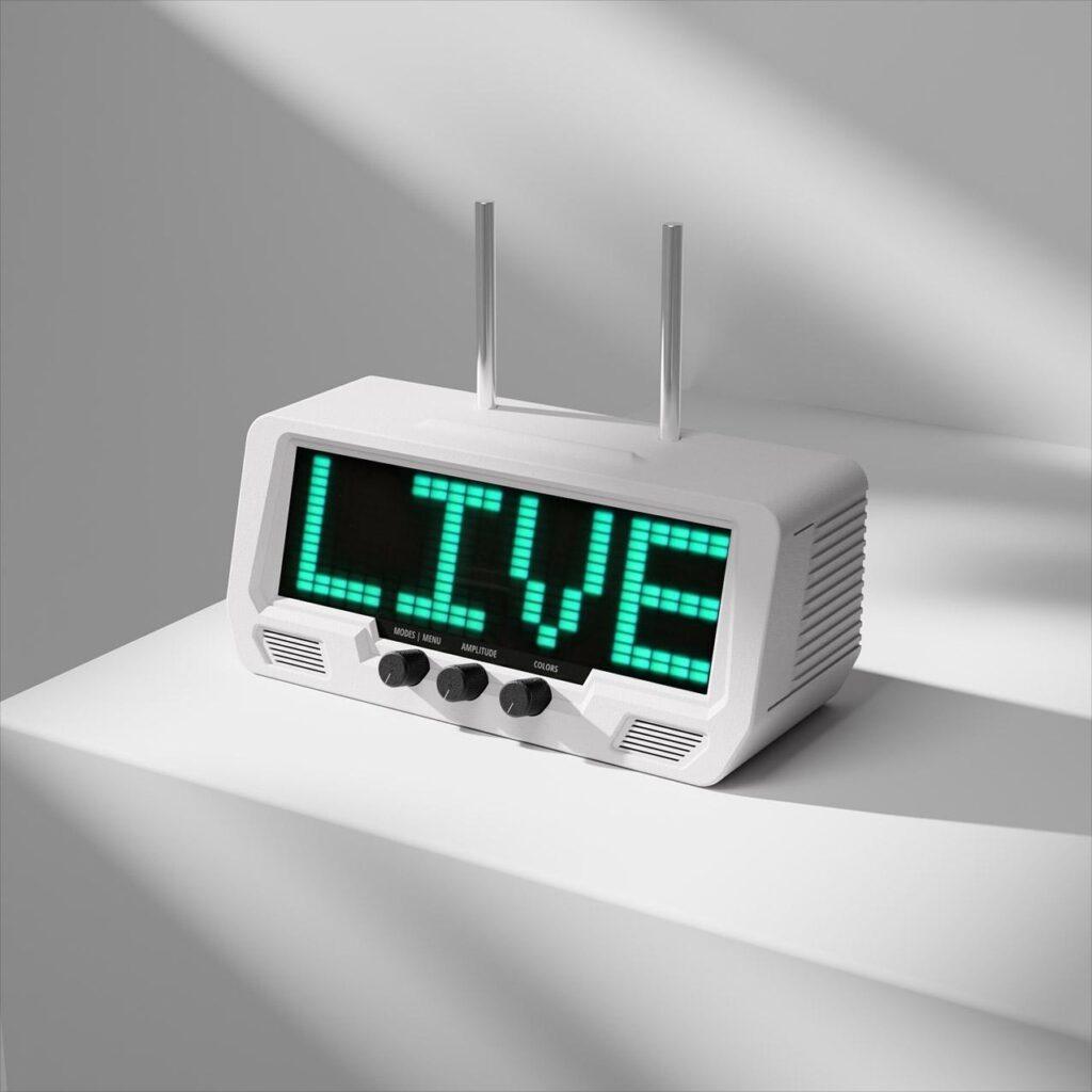 A white digital radio receiver shows "LIVE" in large green LED letters on its LCD screen, sitting on a white surface with bold shadows.