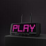 A matte-black stereo receiver with a digital pink LED display reading PLAY, sits on an audio rack against a shadowy background.